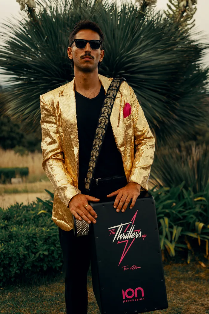 A Thrillers musician in a gold sequin jacket playing the branded Thrillers cajon