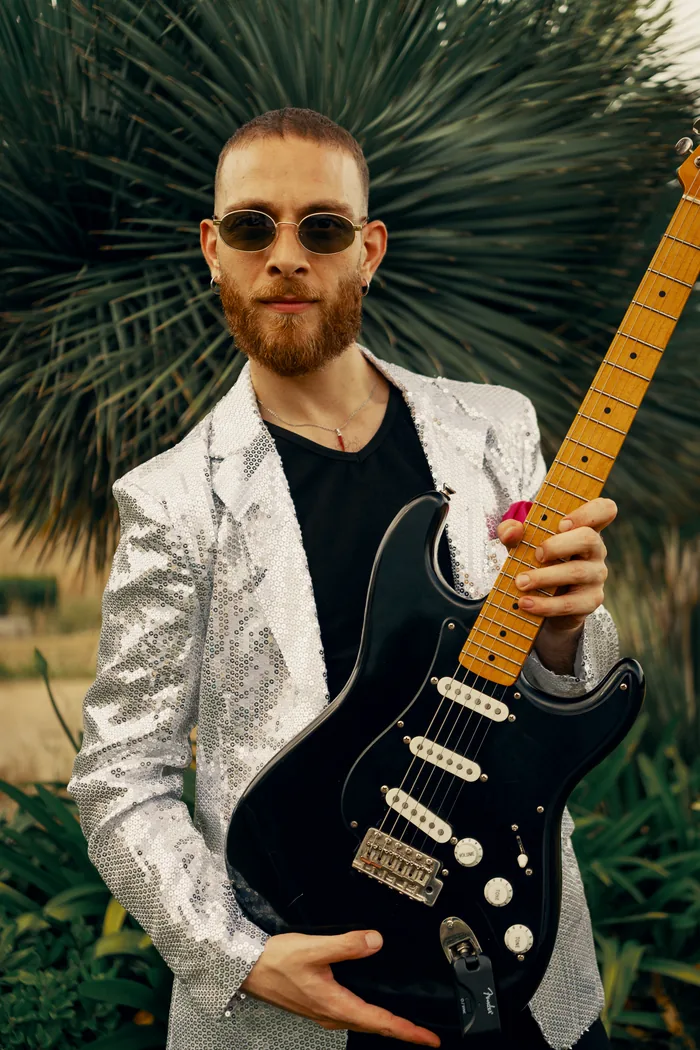 A Thrillers guitarist in a silver sequin blazer holding up his black electric guitar