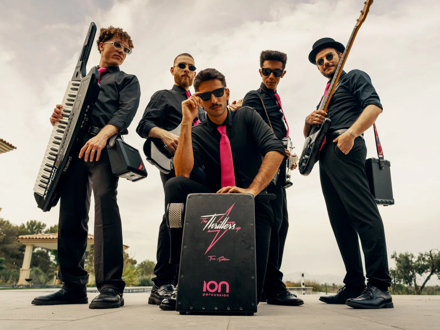 The five members of The Thrillers electric roaming band in black shirts and pink ties, with keytar, guitars and their branded cajon